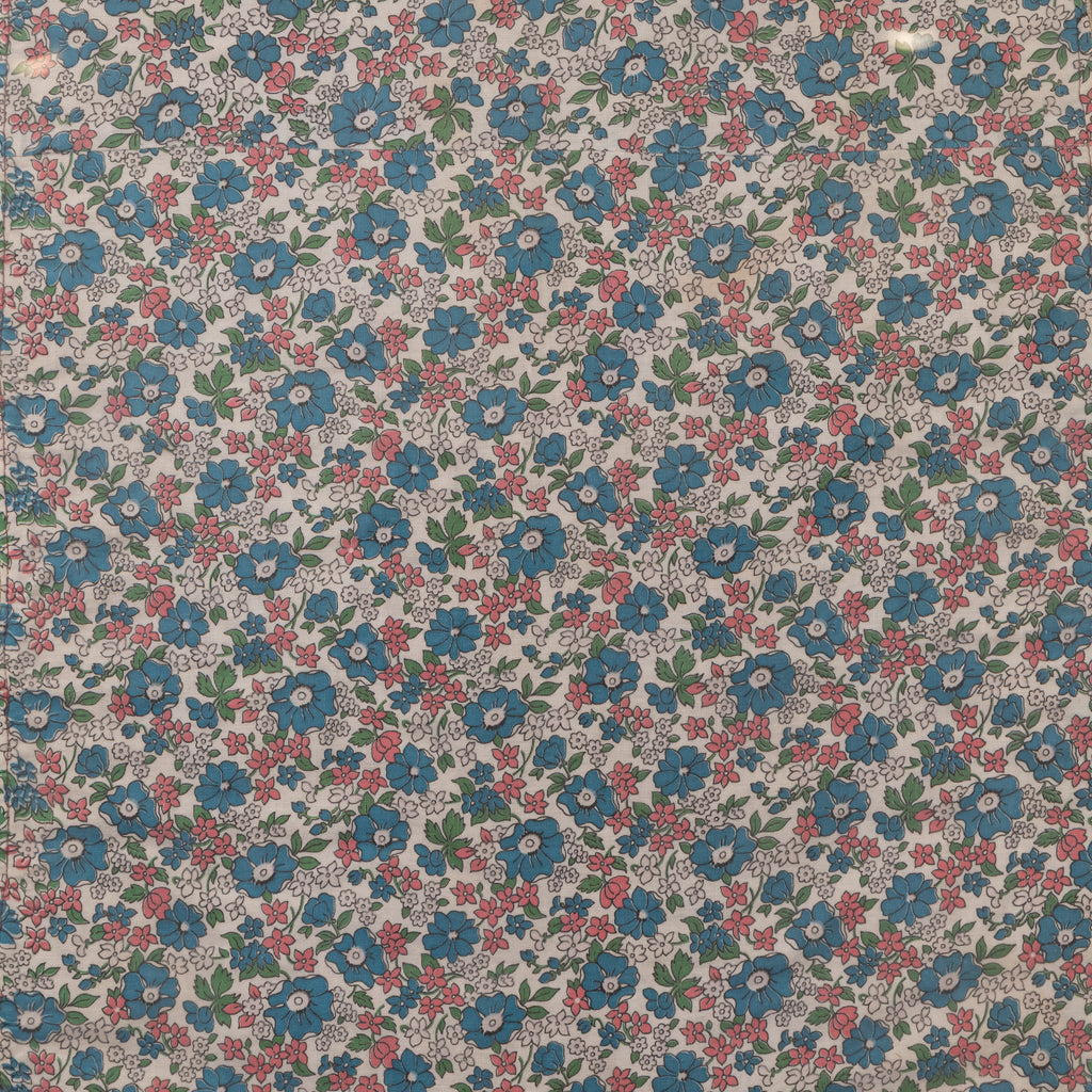A close-up of a repeating floral fabric pattern with blue flowers, pink blossoms, green leaves, and small white centers on a light beige background.