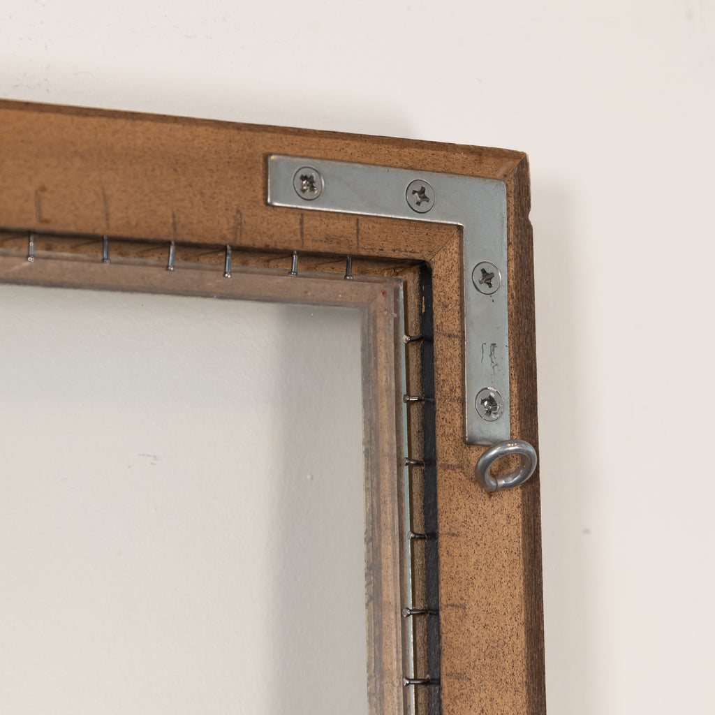 Close-up of a rustic brown wooden picture frame corner with a silver metal L-bracket and hanging ring against a plain off-white wall.