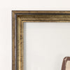 Close-up of a decorative picture frame corner with a distressed metallic gold and bronze finish, set against a plain off-white wall.