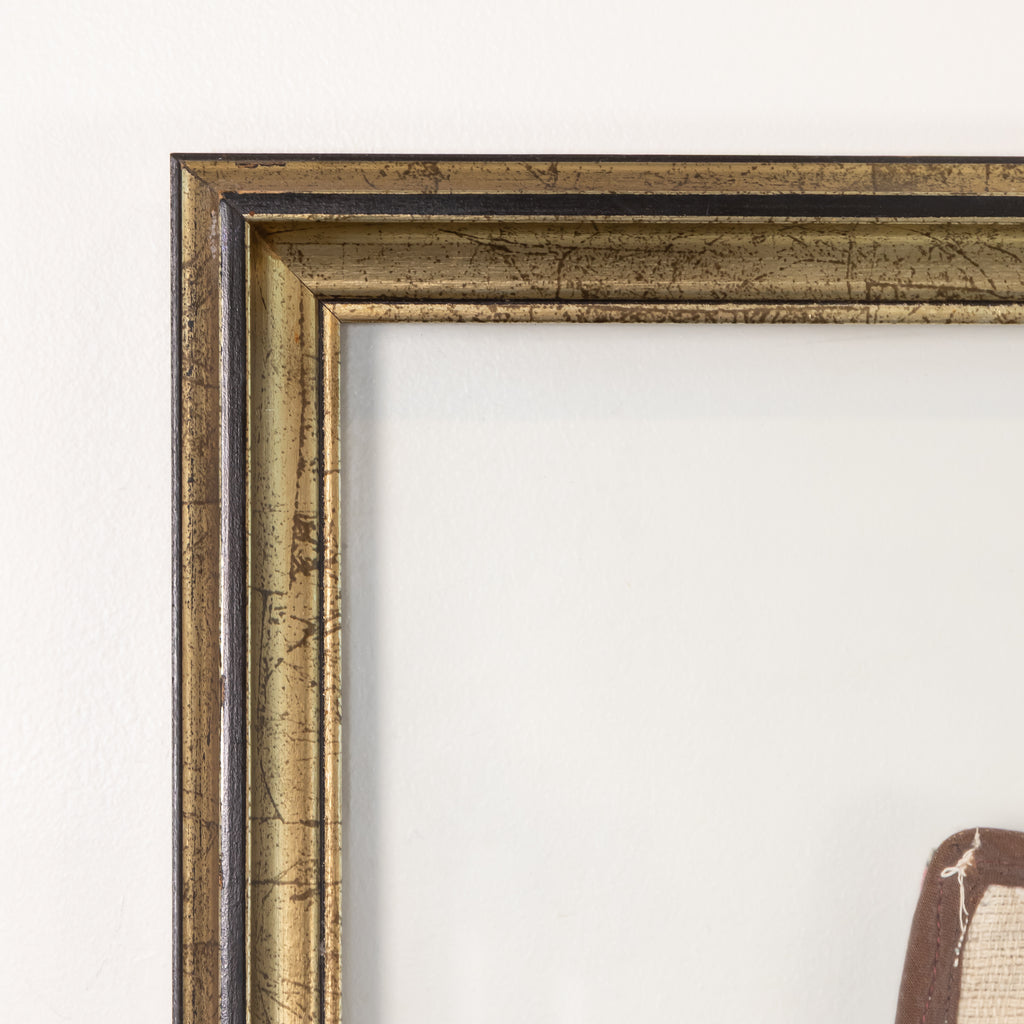 Close-up of a decorative picture frame corner with a distressed metallic gold and bronze finish, set against a plain off-white wall.