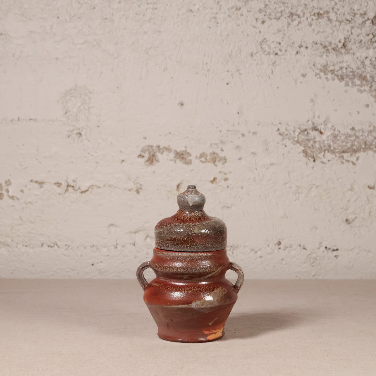 Ceramic jar with a lid on a textured surface with a neutral background