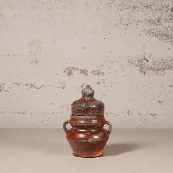 Ceramic jar with a lid on a textured surface with a neutral background