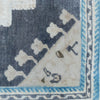 Close-up of an antique rug corner showing a dark navy blue field, a cream-colored section with geometric motifs, and a light blue patterned border.