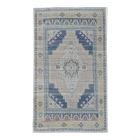 A rectangular area rug with a distressed traditional pattern, featuring a central medallion and geometric borders in shades of blue, beige, and cream on a white background.