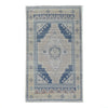 A rectangular area rug with a distressed traditional pattern, featuring a central medallion and geometric borders in shades of blue, beige, and cream on a white background.