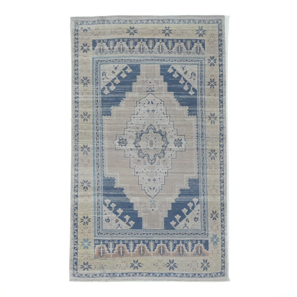 A rectangular area rug with a distressed traditional pattern, featuring a central medallion and geometric borders in shades of blue, beige, and cream on a white background.