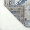 A close-up of a patterned area rug corner folded over to show the underside, featuring a distressed traditional design in beige, blue, and gray tones on a white background.