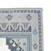 Close-up corner view of a patterned area rug showing a light gray base with blue and dark gray geometric and floral motifs, plus a cream section in the lower left.