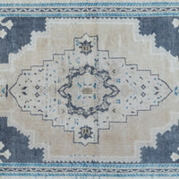 A close-up of a distressed traditional area rug featuring a central medallion design in beige, navy blue, and light blue.