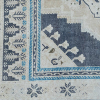 Close-up of a rug corner showing a cream field with a dark navy corner motif, blue and cream border stripes, and small floral/star motifs near the edge.