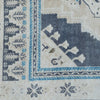 Close-up of a rug corner showing a cream field with a dark navy corner motif, blue and cream border stripes, and small floral/star motifs near the edge.