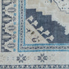 Close-up of a woven rug corner showing cream, navy, and light blue patterned sections with geometric and floral motifs.