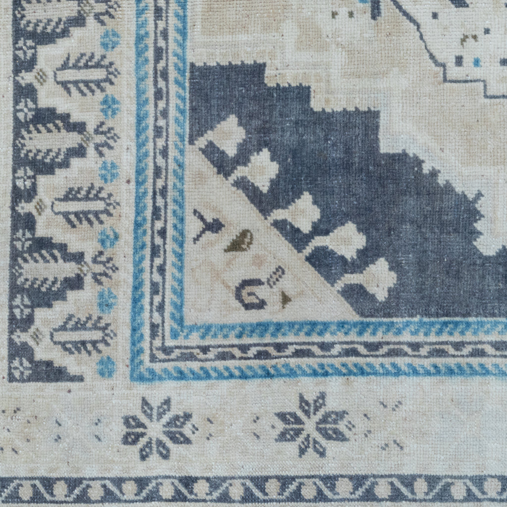 Close-up of a woven rug corner showing cream, navy, and light blue patterned sections with geometric and floral motifs.