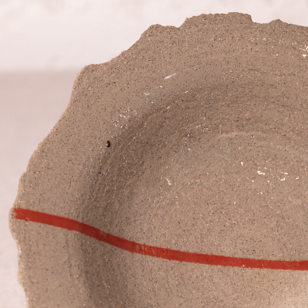 Close-up of a textured ceramic bowl or dish with a speckled taupe-brown glaze and a curved red painted line near the bottom.