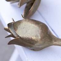 A close-up of a metallic bronze-toned flower bud sculpture resting on a white painted wooden surface.