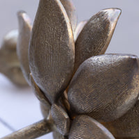 Close-up of a metallic lotus flower sculpture with textured bronze-toned petals on a light gray background.