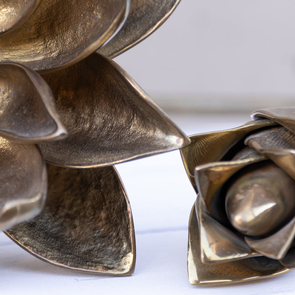 Close-up of metallic bronze sculptural flower petals on a white surface, showing textured metal surfaces and a polished central sphere.