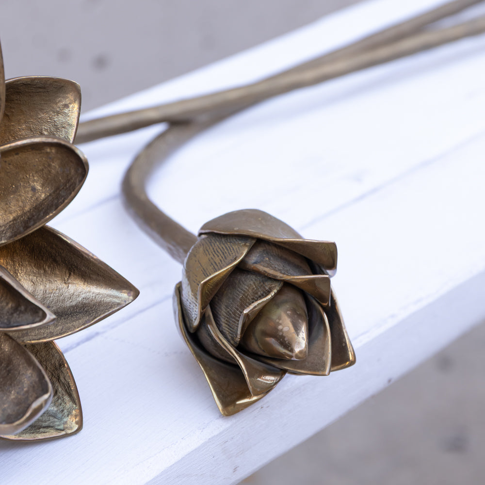 Bronze metal flower stem sculpture with textured petals, resting on a white wooden surface.