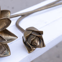 Bronze metal flower stem sculpture with textured petals, resting on a white wooden surface.