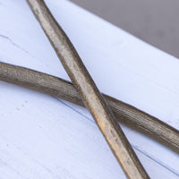 Two metallic bronze-finished rods or bars crossed over a white painted wooden surface.