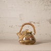 Ceramic teapot with wicker handle on a textured surface