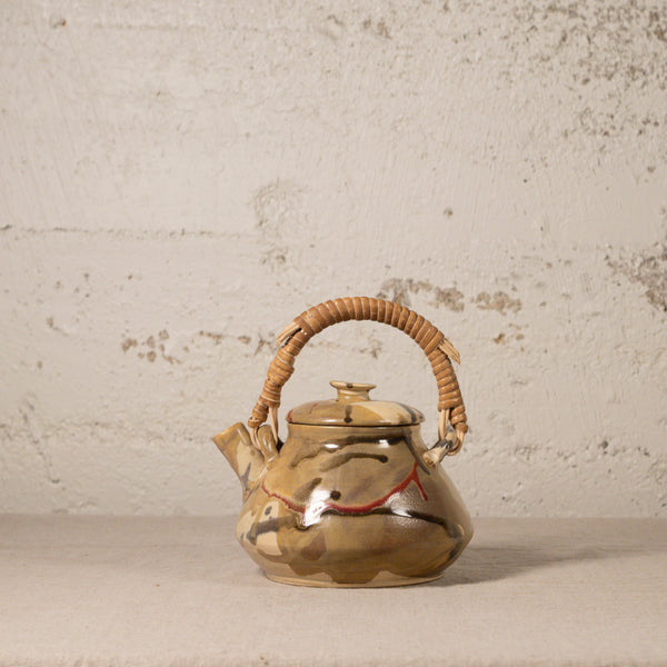 Ceramic teapot with wicker handle on a textured surface