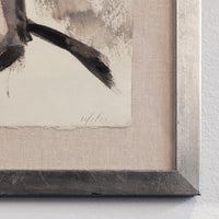 Close-up of framed wall art showing part of an abstract painting with dark brushstrokes on textured off-white paper, set in a light beige mat and a dark gray wood frame against a white wall.