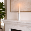 White candle on a marble fireplace mantel with a fire burning below