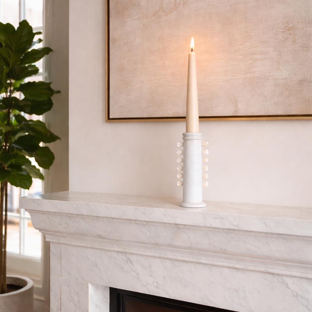 White candle on a marble fireplace mantel with a fire burning below