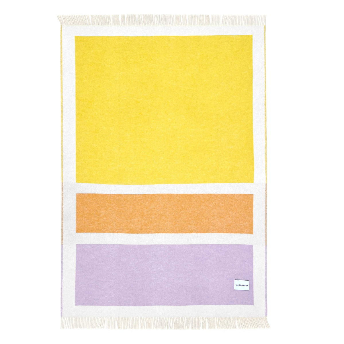 A rectangular woven throw blanket with white fringe on the top and bottom, featuring a minimalist geometric pattern of a large yellow block, a middle orange block, and a bottom lavender block, separated by white borders. A small white tag is visible in the bottom right corner of the lavender section.