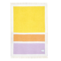 A rectangular woven throw blanket with white fringe on the top and bottom, featuring a minimalist geometric pattern of a large yellow block, a middle orange block, and a bottom lavender block, separated by white borders. A small white tag is visible in the bottom right corner of the lavender section.
