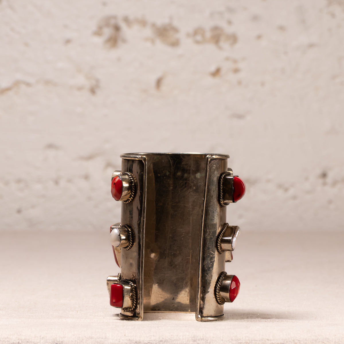 A wide silver cuff bracelet featuring four red faceted gemstones set in silver bezel settings, displayed against a textured off-white background.