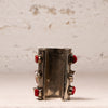 A wide silver cuff bracelet featuring four red faceted gemstones set in silver bezel settings, displayed against a textured off-white background.