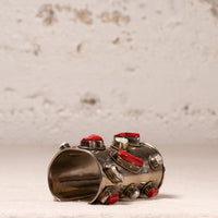 A wide silver cuff bracelet decorated with multiple red cabochon stones and textured silver bezel settings, photographed on a light textured surface with a neutral background.