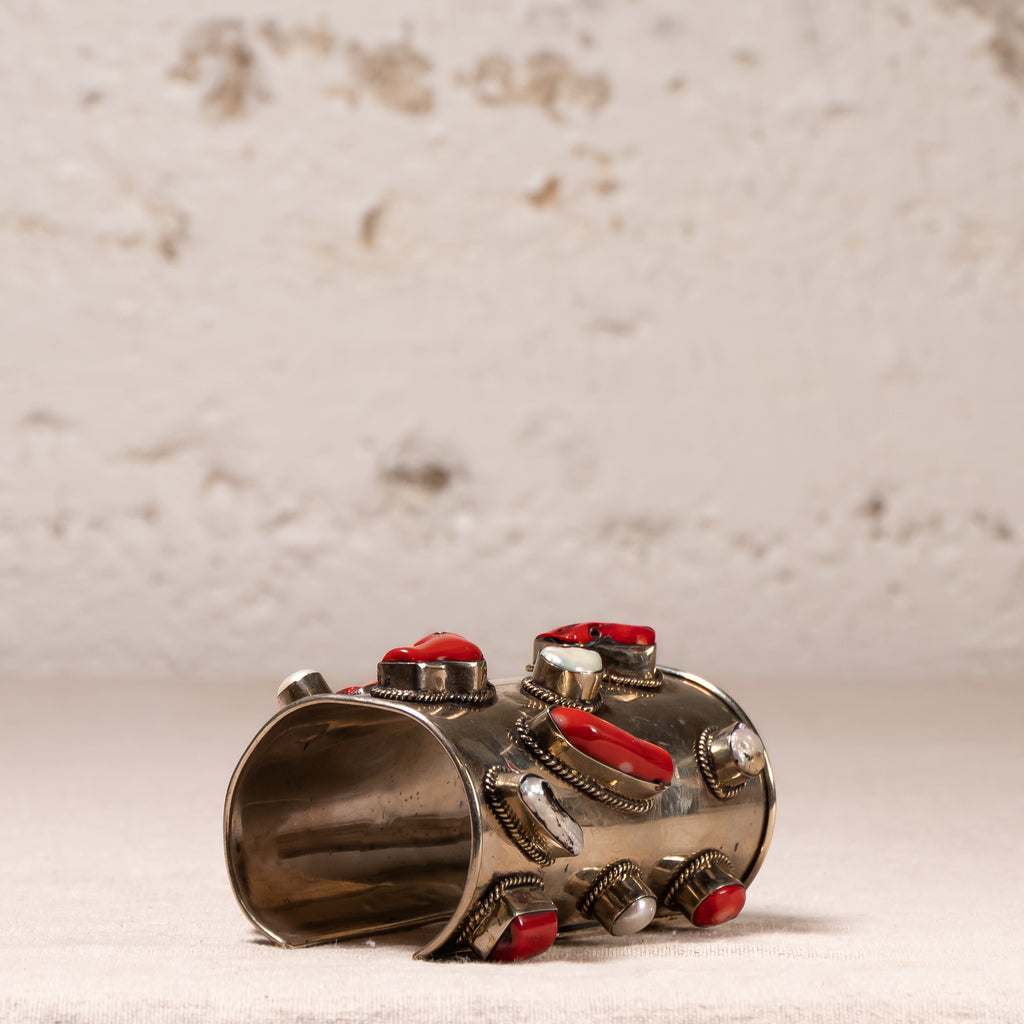 A wide silver cuff bracelet decorated with multiple red cabochon stones and textured silver bezel settings, photographed on a light textured surface with a neutral background.