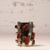 A vintage silver cuff bracelet decorated with red coral inlays and small white pearl accents, displayed against a textured beige background.