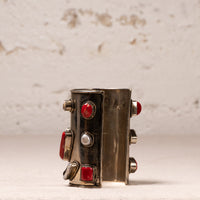A wide silver cuff bracelet decorated with red gemstones and a central white pearl, displayed on a light textured surface against a neutral background.