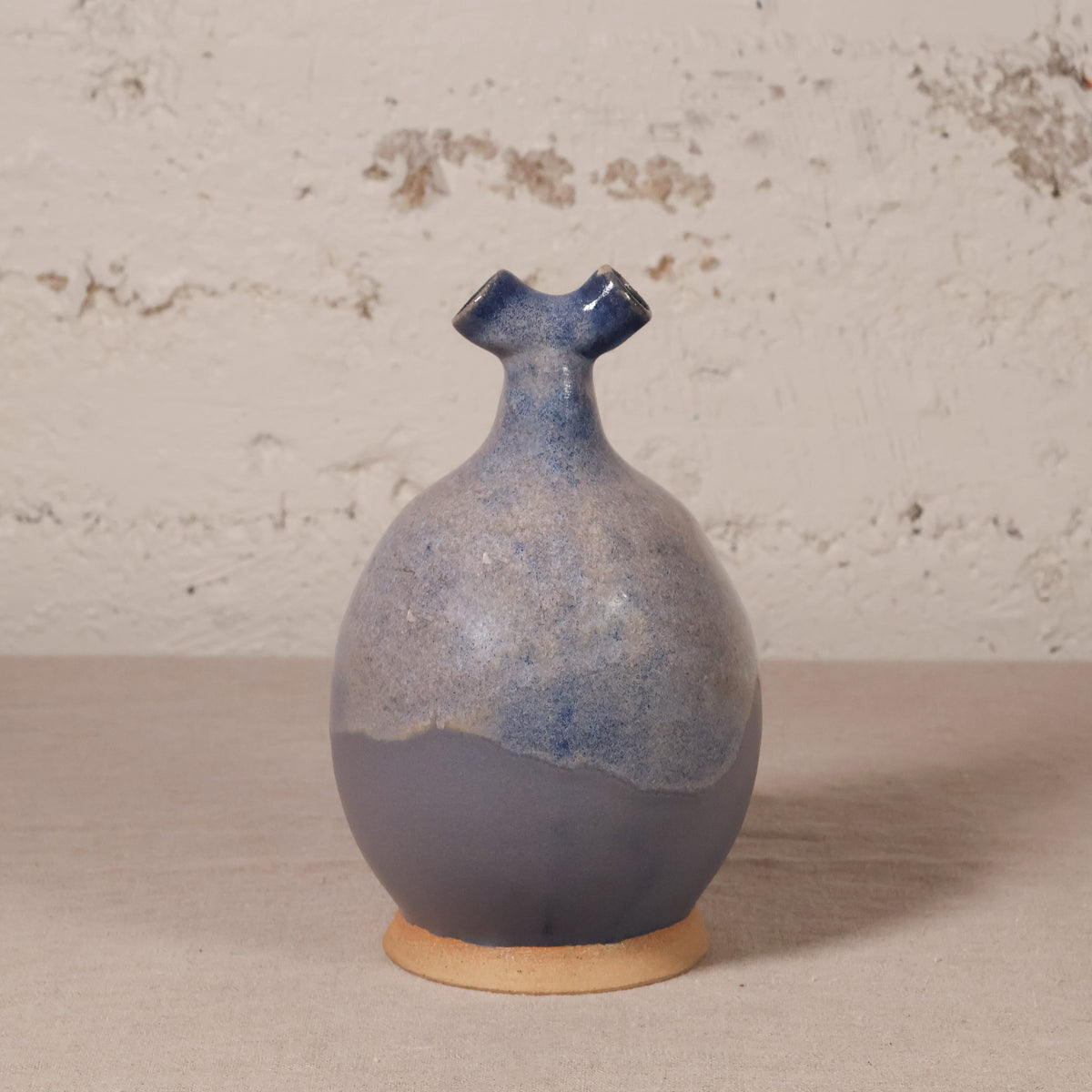 Ceramic vase with blue and beige glaze on a textured surface