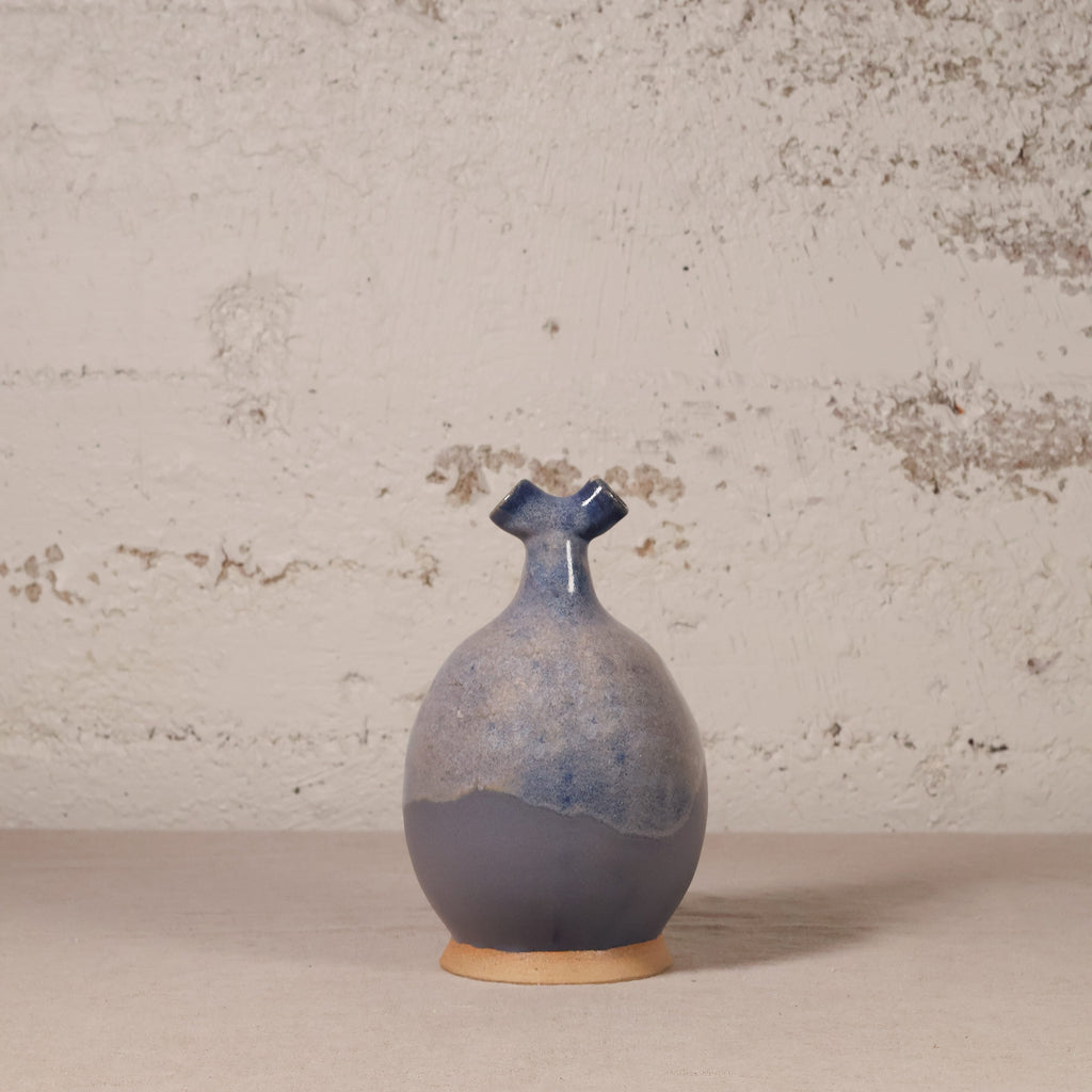 Blue ceramic vase on a beige surface with a textured wall background