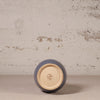 Ceramic vase with a blue exterior and beige interior on a textured surface.