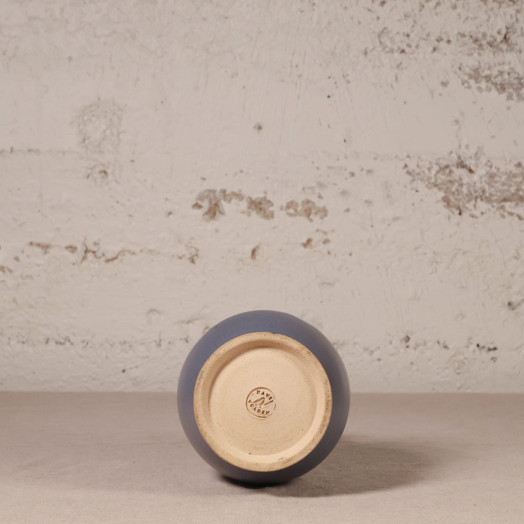 Ceramic vase with a blue exterior and beige interior on a textured surface.