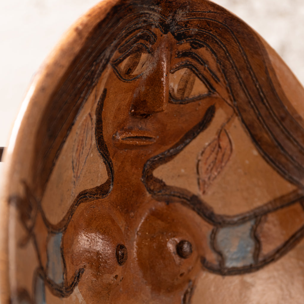 Close-up of a terracotta-colored ceramic sculpture depicting a stylized female face and upper torso with dark brown linework and small light blue accents.