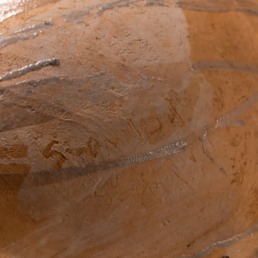 Close-up of a terracotta clay surface with a glossy, wet sheen and visible horizontal metallic silver lines.