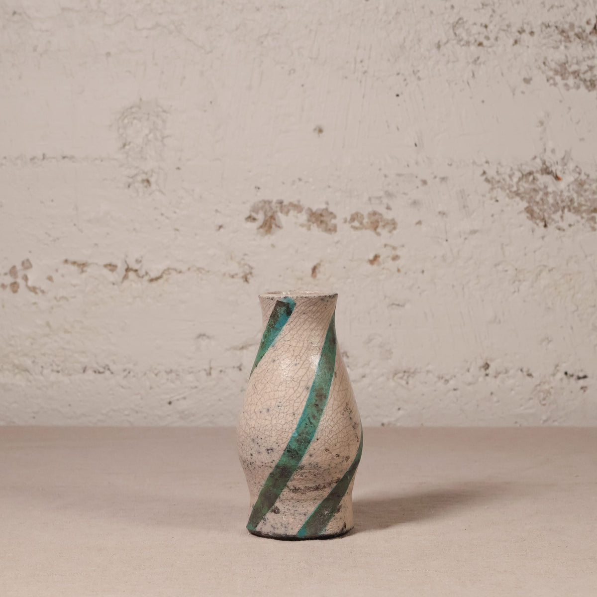 Ceramic vase with green stripes on a textured surface and wall background