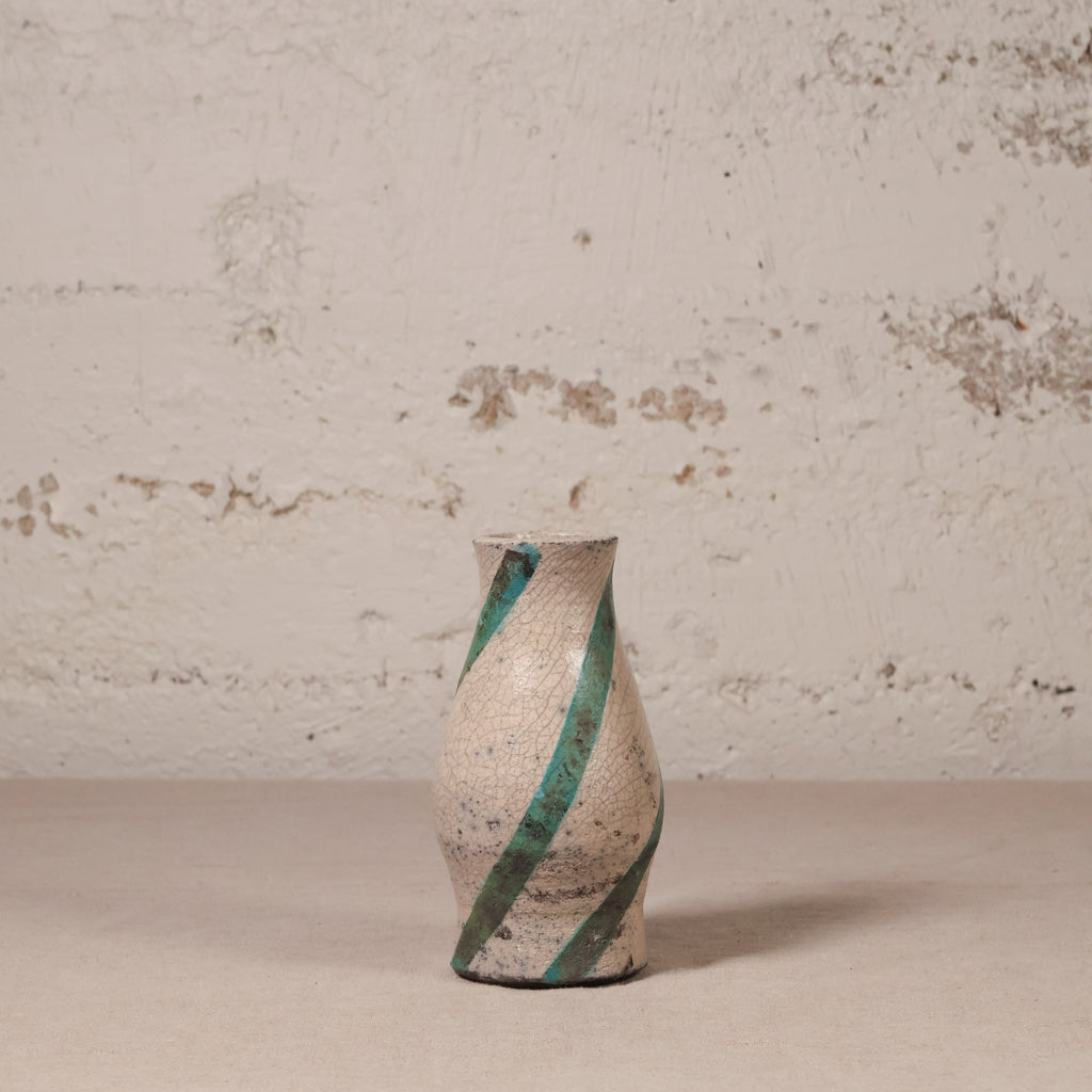Ceramic vase with green stripes on a textured surface and wall background