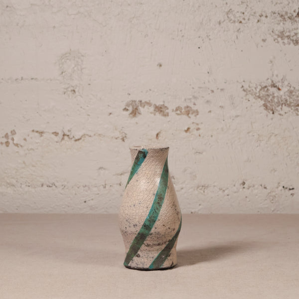 Ceramic vase with green stripes on a textured surface and wall background