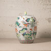 Decorative ceramic jar with colorful floral and bird design on a textured surface.