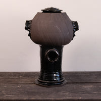 A handmade ceramic vessel with a rounded, bulbous body, a glossy black base, and side handles, sitting on a dark wooden surface against a plain light background.