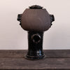 A handmade ceramic vessel with a rounded, bulbous body, a glossy black base, and side handles, sitting on a dark wooden surface against a plain light background.