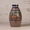 A vintage ceramic vase with a bulbous shape, featuring a hand-painted floral and bird design in blue, green, and brown on a beige stoneware base, set against a textured off-white wall.